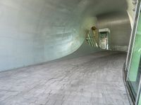 a large white tunnel with concrete floor next to it and glass doors around it in a concrete surfaced hallway