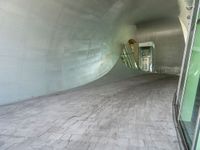 a large white tunnel with concrete floor next to it and glass doors around it in a concrete surfaced hallway