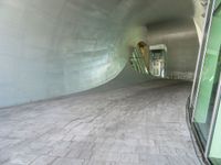 a large white tunnel with concrete floor next to it and glass doors around it in a concrete surfaced hallway