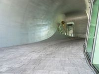 a large white tunnel with concrete floor next to it and glass doors around it in a concrete surfaced hallway