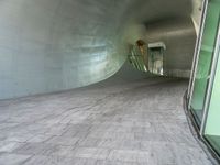 a large white tunnel with concrete floor next to it and glass doors around it in a concrete surfaced hallway