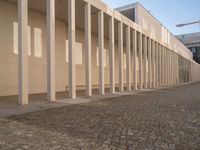 a very long brick walkway leading to a building with columns in it in front of the outside wall