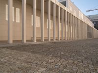 a very long brick walkway leading to a building with columns in it in front of the outside wall