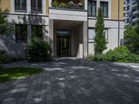 a residential driveway with a bench and bushes in between buildings and green grass on either side