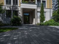 a residential driveway with a bench and bushes in between buildings and green grass on either side