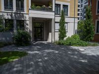 a residential driveway with a bench and bushes in between buildings and green grass on either side