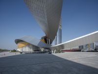 an empty concrete plaza with a futuristic building in the background and a blue sky overhead