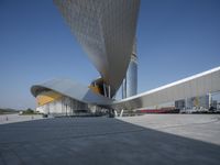 an empty concrete plaza with a futuristic building in the background and a blue sky overhead