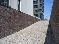 an alley way with brick pavement between the brick walls and building on the left, and a side walk to another