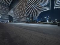 this is an empty concrete floor at night, near a tall building with futuristic architecture