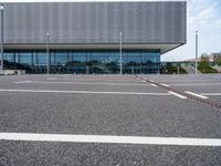 a parking lot with a light post on the corner and an outside building with a glass - walled facade