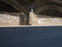 graffiti covered brick wall and gate under an overpass in an urban area with sun light