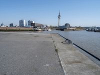 a bike leaning against an outdoor bench by a body of water with city buildings in the background