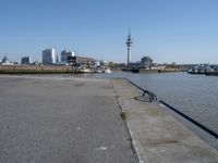 a bike leaning against an outdoor bench by a body of water with city buildings in the background