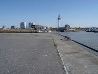 a bike leaning against an outdoor bench by a body of water with city buildings in the background