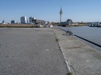 a bike leaning against an outdoor bench by a body of water with city buildings in the background