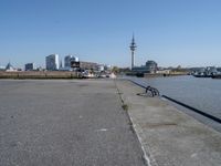 a bike leaning against an outdoor bench by a body of water with city buildings in the background