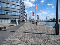 a cobble stone street with a few tall buildings behind it in the distance is a large riverfront