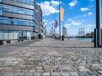 a cobble stone street with a few tall buildings behind it in the distance is a large riverfront