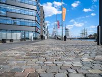 a cobble stone street with a few tall buildings behind it in the distance is a large riverfront