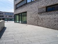 a brick and glass walkway near building windows on a sunny day in a city with no one going