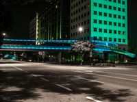 a bright lit up pedestrian bridge over an empty road at night in the city with cars going by