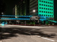 a bright lit up pedestrian bridge over an empty road at night in the city with cars going by