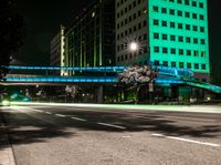 a bright lit up pedestrian bridge over an empty road at night in the city with cars going by