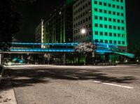 a bright lit up pedestrian bridge over an empty road at night in the city with cars going by