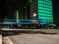 a bright lit up pedestrian bridge over an empty road at night in the city with cars going by