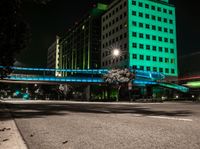 a bright lit up pedestrian bridge over an empty road at night in the city with cars going by