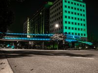 a bright lit up pedestrian bridge over an empty road at night in the city with cars going by