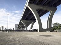 the sidewalk in a parking lot next to a bridge over water and some tall buildings