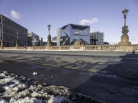 a building with a large sculpture on the street with snowy ground below it and buildings behind it