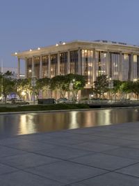 the walkway at the park leads to a lake and buildings in the background as evening falls