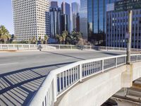 the sun reflects on a street with large buildings in the background and a view of a bridge in the foreground