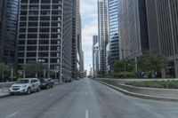 the view of a downtown street with cars passing by on either side of it and skyscrapers,