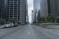 the view of a downtown street with cars passing by on either side of it and skyscrapers,