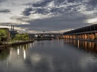 the water is flowing under a bridge near buildings at dusk and reflecting the sky with the lights