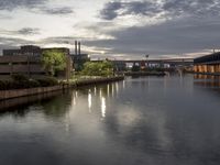 the water is flowing under a bridge near buildings at dusk and reflecting the sky with the lights