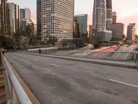 a wide open freeway, with tall buildings along both sides and on both side of it, are lit at dusk