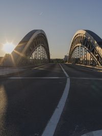 the sun is setting on an empty highway near a large bridge that crosses a river