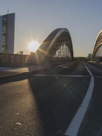 the sun is setting on an empty highway near a large bridge that crosses a river