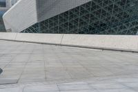 a boy with a skateboard on the ground outside a building with a glass roof