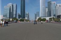 a group of people walking down the middle of a street near tall buildings in the background