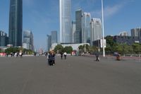 a group of people walking down the middle of a street near tall buildings in the background