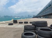 many tires have been set up along the walkway on a dock by a harbor with a cityscape in the background