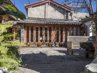 a building with wooden doors, windows and plants in the front of it and a few chairs