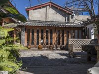 a building with wooden doors, windows and plants in the front of it and a few chairs