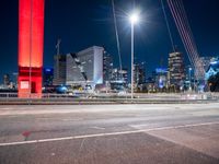 the city skyline is illuminated at night from under the bridge on a street in front of the road is a busy highway